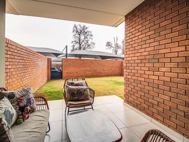 A covered patio area featuring tiled flooring and exposed brick walls, overlooking a private garden space with perimeter brick walling.