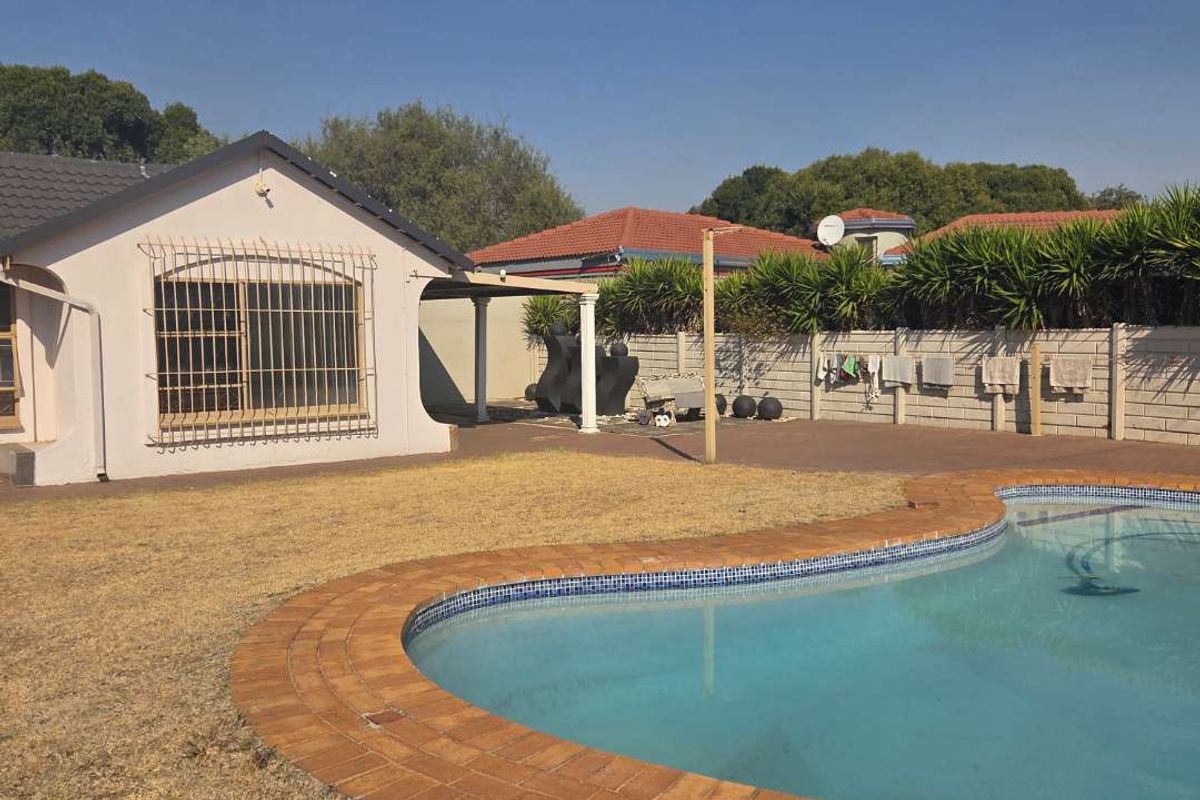 Rear exterior view featuring a swimming pool with brick coping, a covered patio area, and a precast concrete boundary wall.