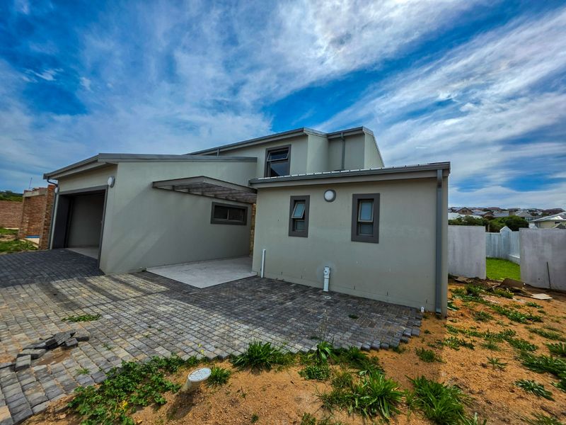 Rear view of the property featuring a paved driveway, attached garage, and modern exterior finishes with unfinished landscaping.