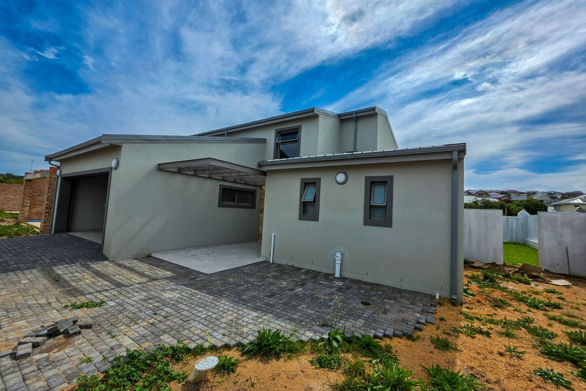 Rear view of the property featuring a paved driveway, attached garage, and modern exterior finishes with unfinished landscaping.