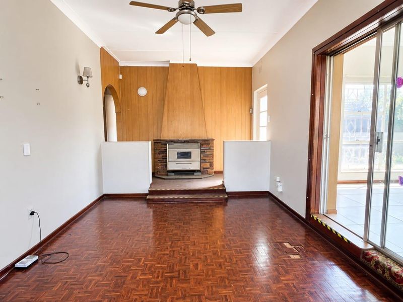 Spacious living room featuring original parquet flooring, a central fireplace with wood paneling, and large sliding glass doors leading to an outdoor area.