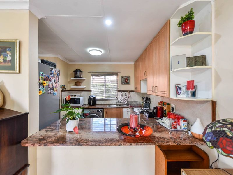 Functional kitchen featuring granite countertops, wooden cabinetry, double basin sink, and tiled backsplash with convenient breakfast bar seating.
