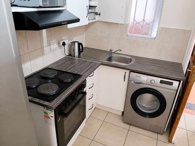 Compact kitchen featuring laminate countertops, built-in cabinetry, an electric hob with oven, extractor fan, and tiled finishes throughout.