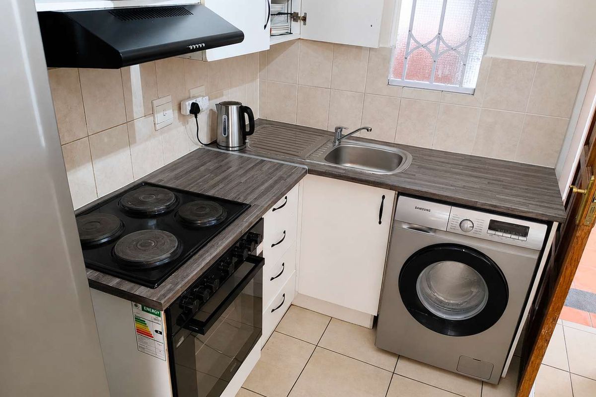 Compact kitchen featuring laminate countertops, built-in cabinetry, an electric hob with oven, extractor fan, and tiled finishes throughout.