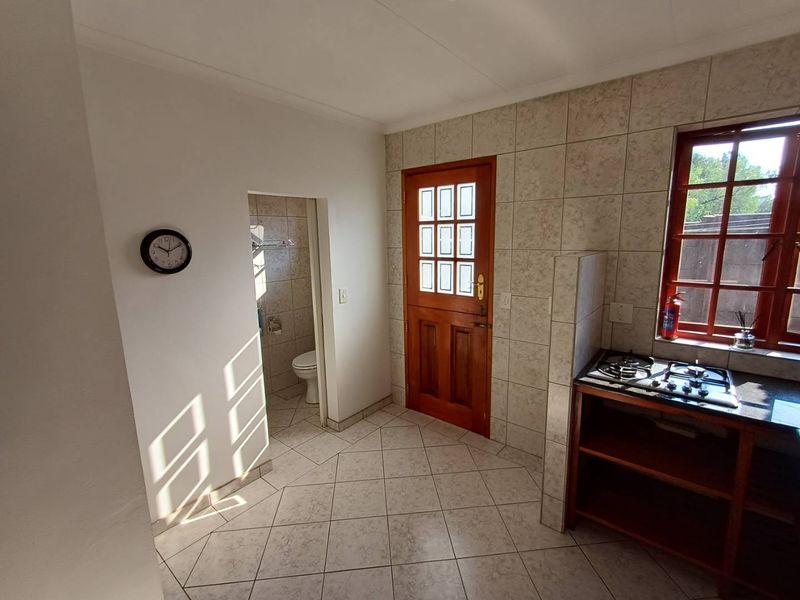 A functional kitchen area featuring tiled flooring, a built-in gas hob, and direct access to an adjacent toilet facility.