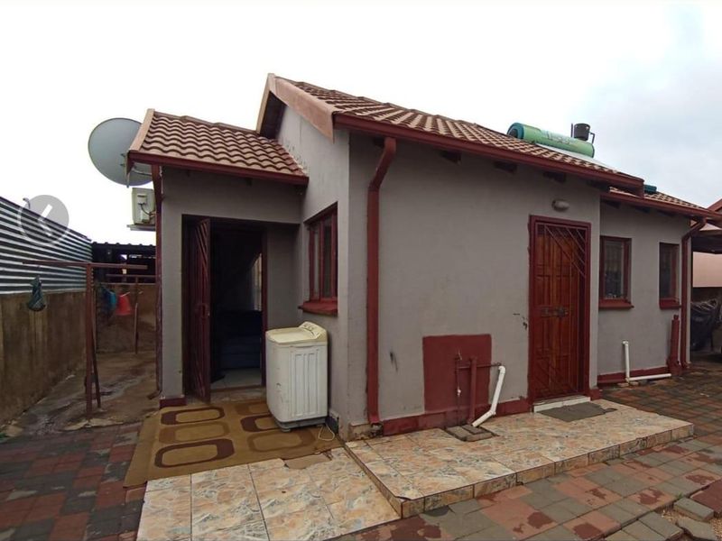 Rear exterior view of the house featuring a tiled roof, solar water heater, and paved patio area with security door access.