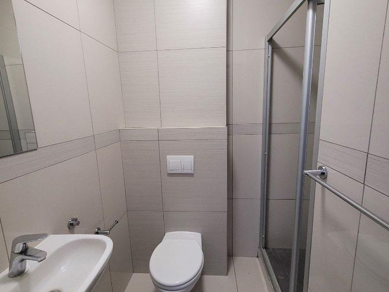 Modern bathroom featuring a wall-mounted toilet, glass shower enclosure, and a sleek ceramic basin with chrome fixtures, finished with neutral wall tiles.