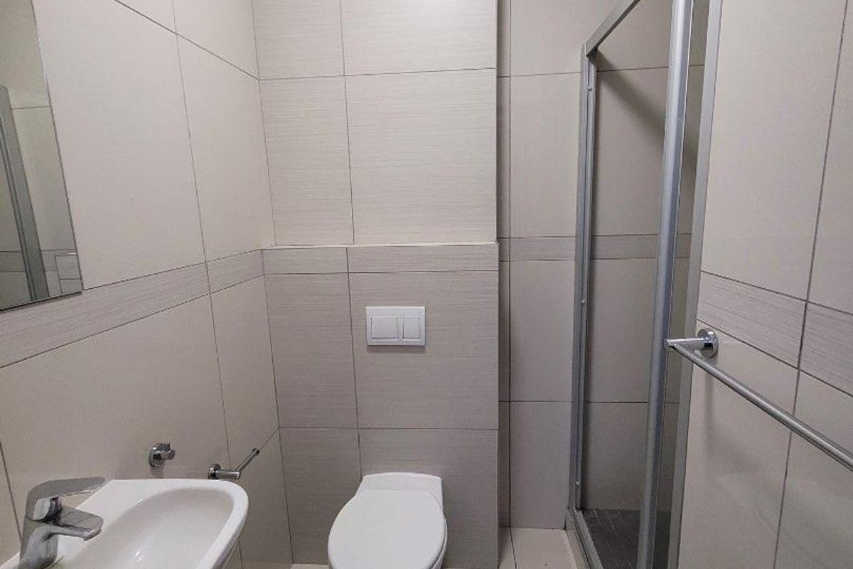 Modern bathroom featuring a wall-mounted toilet, glass shower enclosure, and a sleek ceramic basin with chrome fixtures, finished with neutral wall tiles.