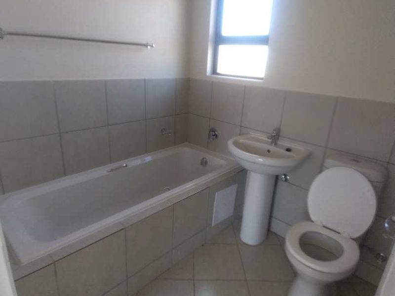 A functional bathroom featuring a bathtub, pedestal basin, and toilet with neutral tiled finishes and natural light.