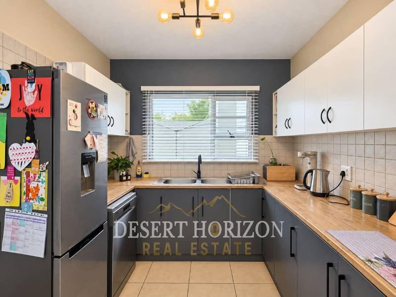 A well-maintained kitchen featuring modern grey and white cabinetry, wooden countertops, a double basin sink, and a tiled backsplash.