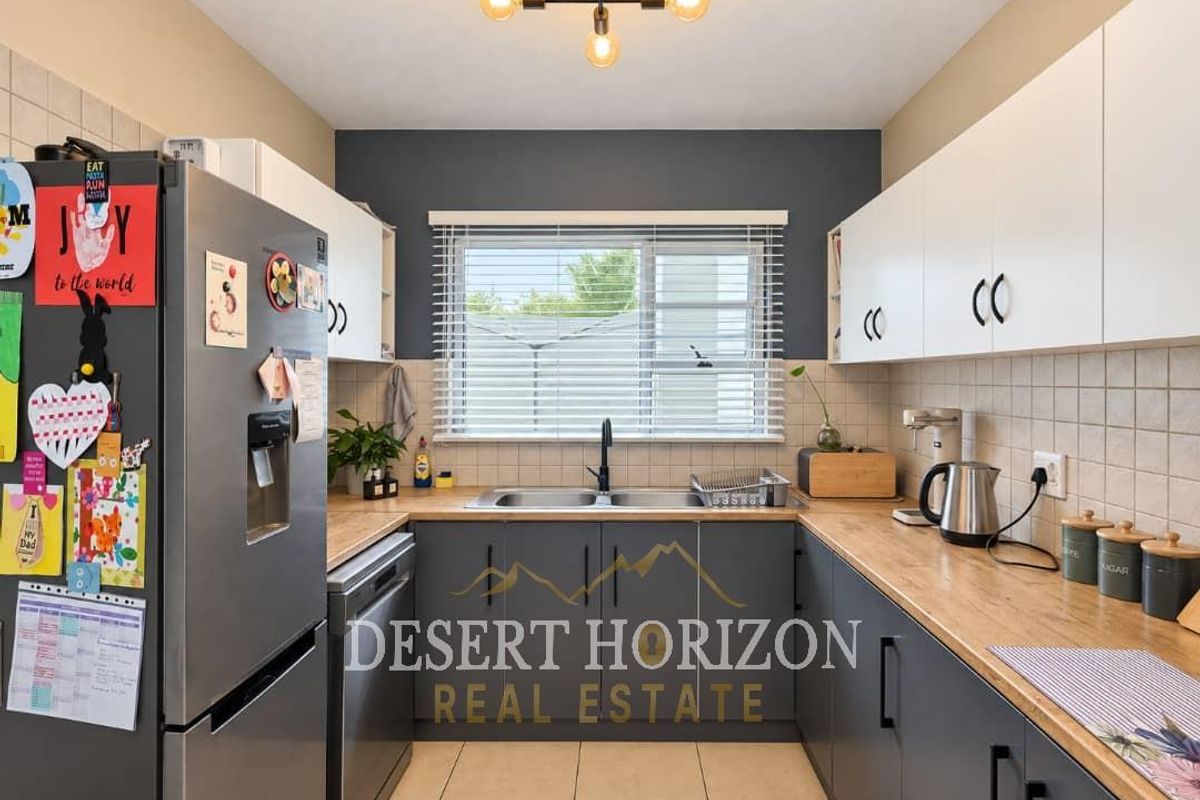 A well-maintained kitchen featuring modern grey and white cabinetry, wooden countertops, a double basin sink, and a tiled backsplash.