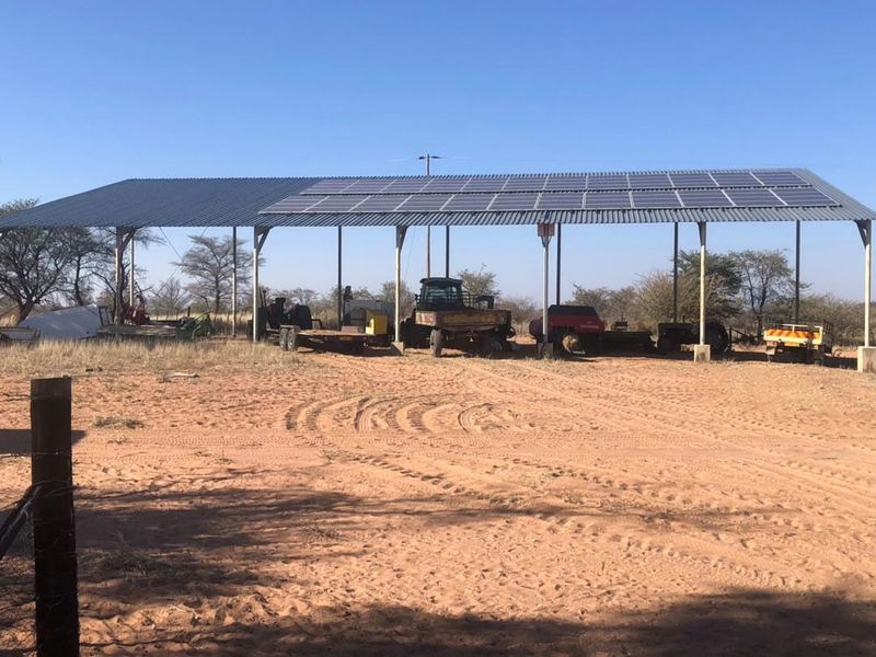A large open-sided farm utility shed featuring a corrugated metal roof equipped with integrated solar panels and sturdy steel support columns.