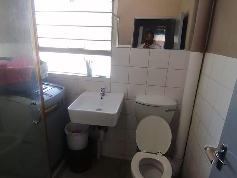 A compact bathroom featuring a wall-mounted basin, toilet, and shower enclosure with tiled finishes and a louvered window.