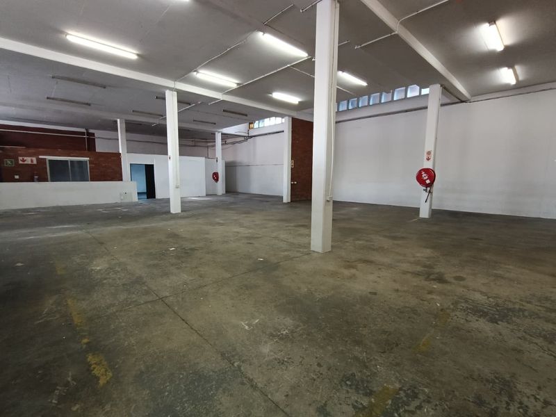 Spacious industrial warehouse area featuring concrete flooring, exposed structural columns, and functional fire safety equipment, suitable for various commercial or storage applications.