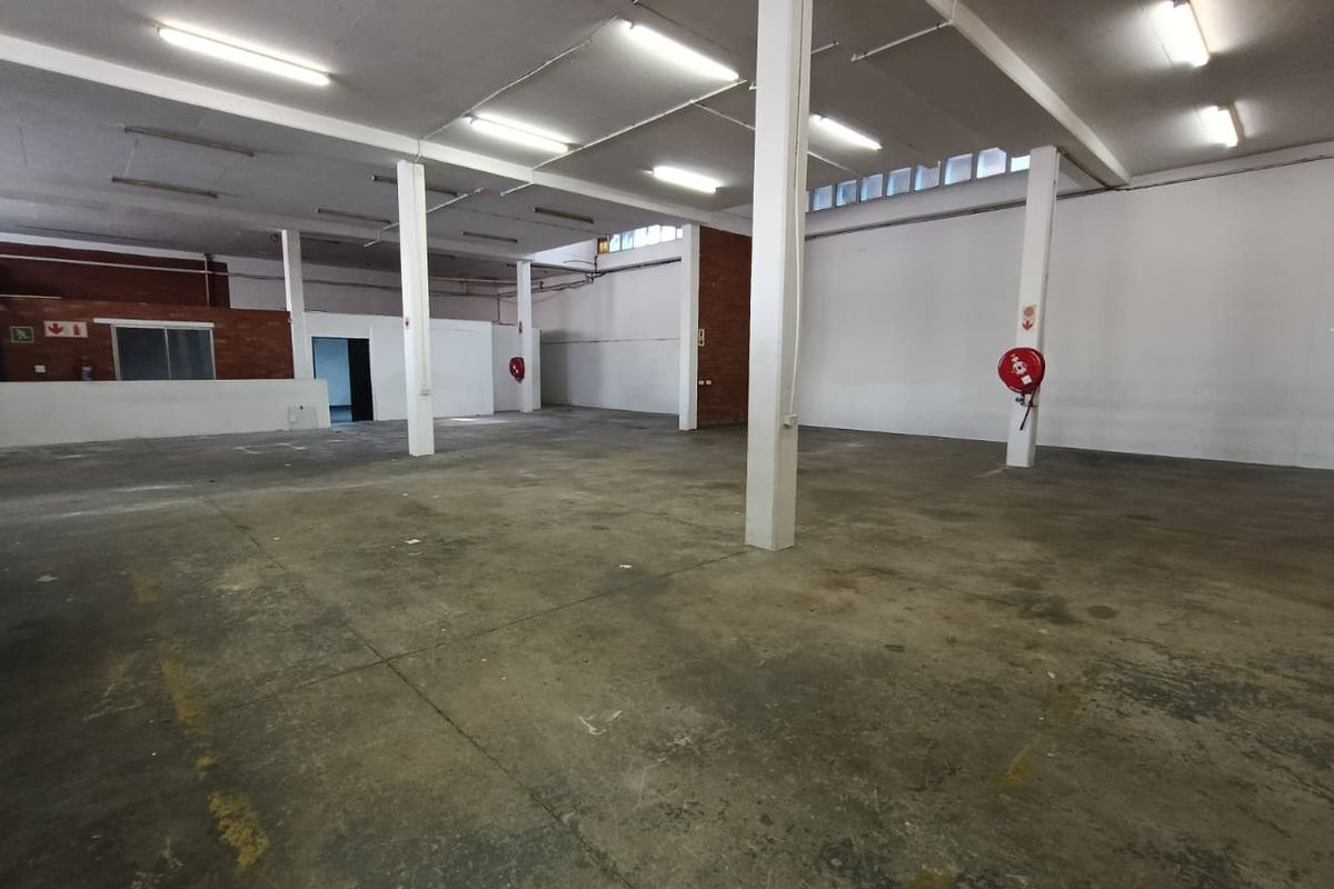 Spacious industrial warehouse area featuring concrete flooring, exposed structural columns, and functional fire safety equipment, suitable for various commercial or storage applications.