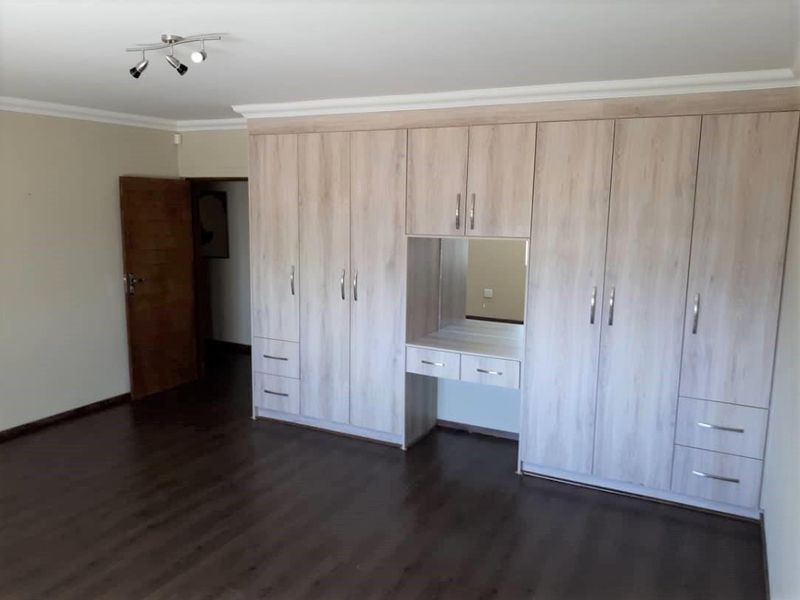 Spacious bedroom featuring extensive light wood-finish built-in cupboards with an integrated vanity station and dark laminate flooring.