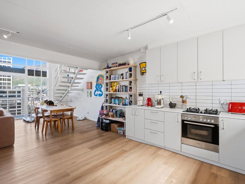 Modern open-plan living area featuring a sleek kitchen with built-in appliances, laminate flooring, and a spiral staircase leading to an upper level.