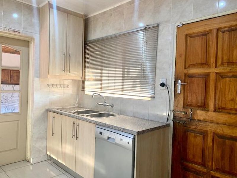 A functional kitchen area featuring light wood cabinetry, a double sink, tiled walls, and a built-in dishwasher.