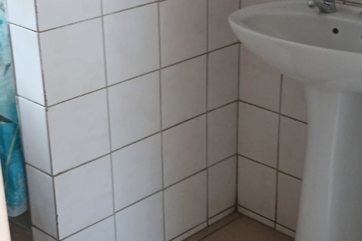 A functional bathroom space featuring a pedestal basin, tiled walls, and tiled flooring, requiring cosmetic updates to improve its overall condition.