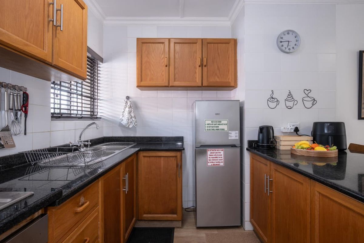 A functional kitchen featuring warm wooden cabinetry, contrasting black granite countertops, and a tiled backsplash, providing a classic and practical workspace.