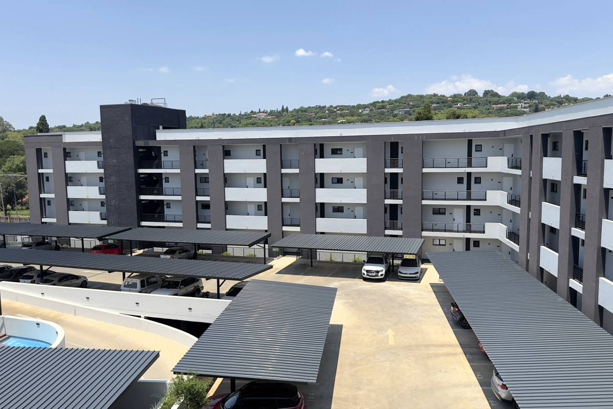 An elevated view of a modern apartment complex featuring multi-level residential units, covered parking bays, and a paved driveway area.