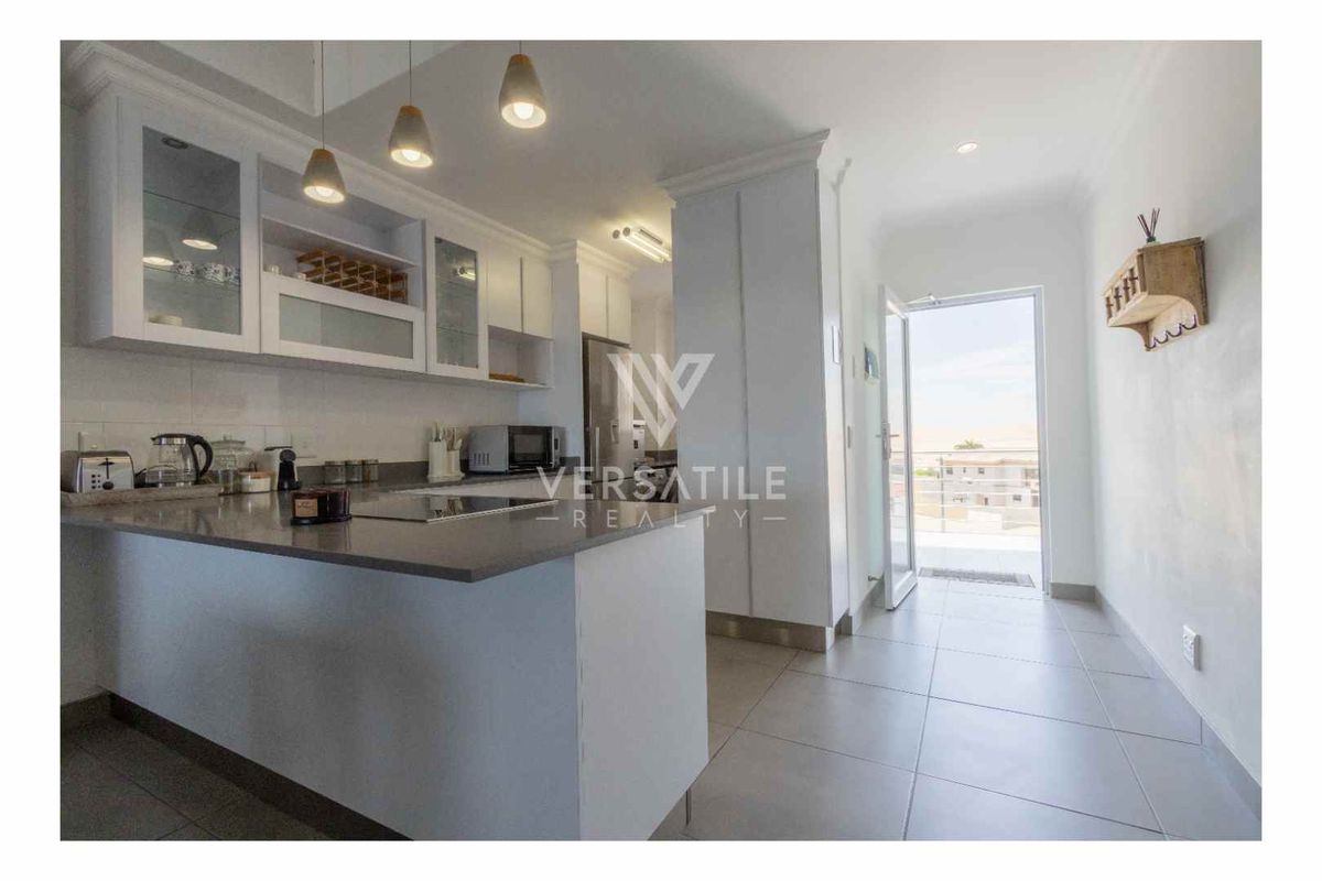 Modern kitchen featuring sleek white cabinetry, stone countertops, and a breakfast bar, with direct access to an outdoor balcony area.