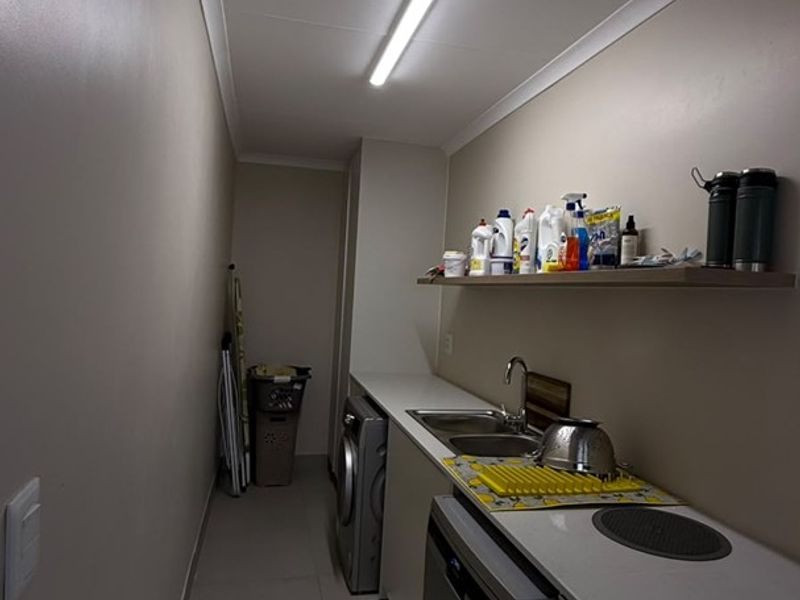 A functional laundry room featuring built-in cabinetry, a stainless steel sink, tiled flooring, and efficient overhead lighting.