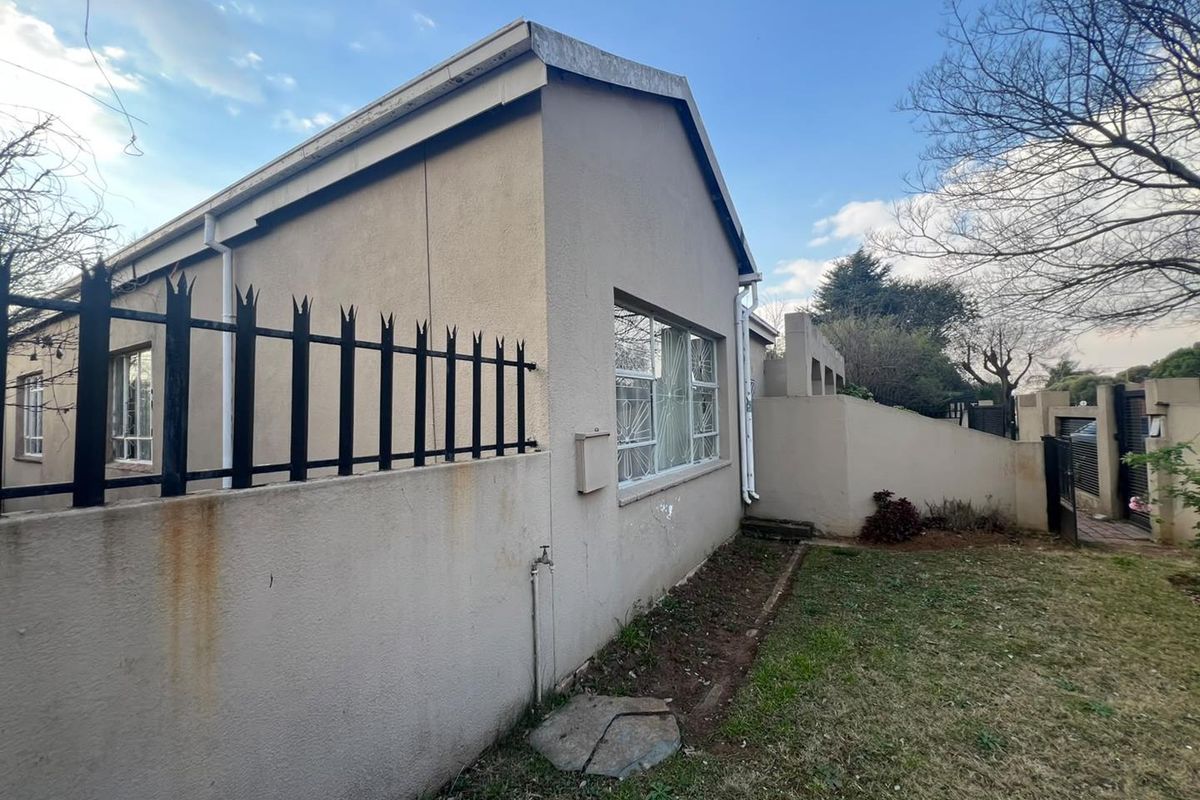 Rear exterior view of the property featuring a perimeter wall with security spikes, external water tap, and established garden area.