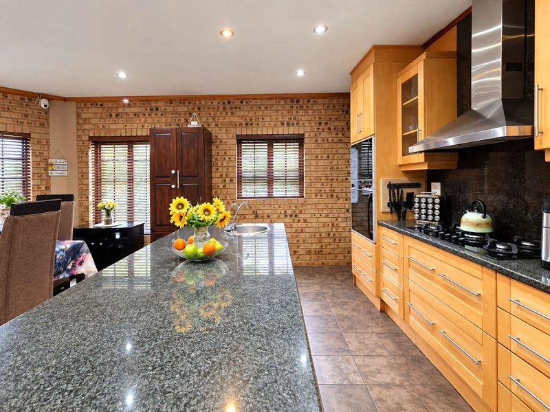 Spacious kitchen featuring warm wooden cabinetry, granite countertops, a gas hob with stainless steel extractor, and a distinctive exposed brick feature wall.