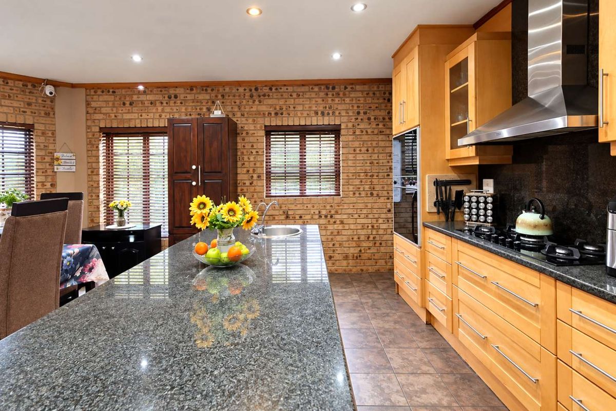 Spacious kitchen featuring warm wooden cabinetry, granite countertops, a gas hob with stainless steel extractor, and a distinctive exposed brick feature wall.