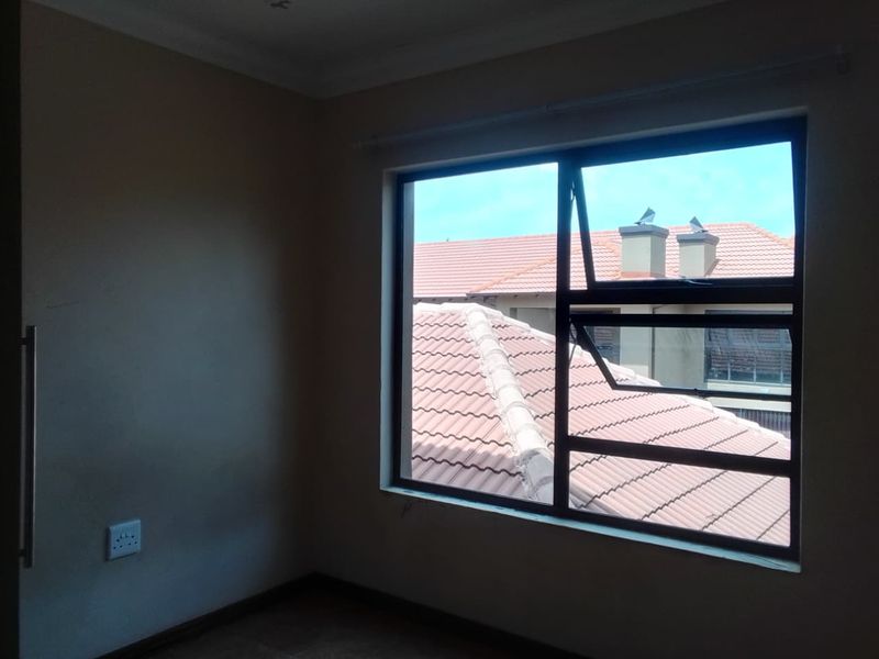 An empty bedroom featuring a large aluminium window with views of neighbouring tiled roofs and a built-in cupboard.