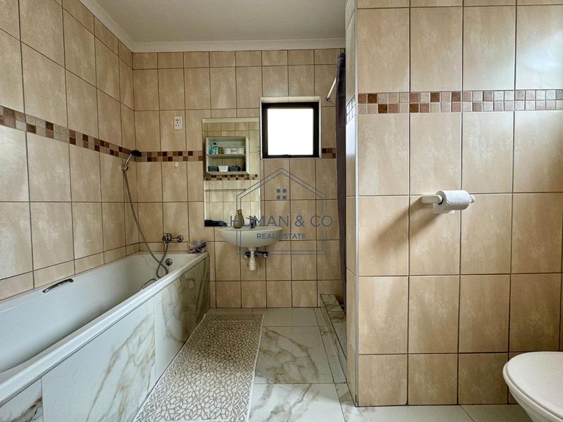 A functional bathroom featuring a bathtub, wall-mounted basin, and toilet with neutral floor-to-ceiling wall tiling.
