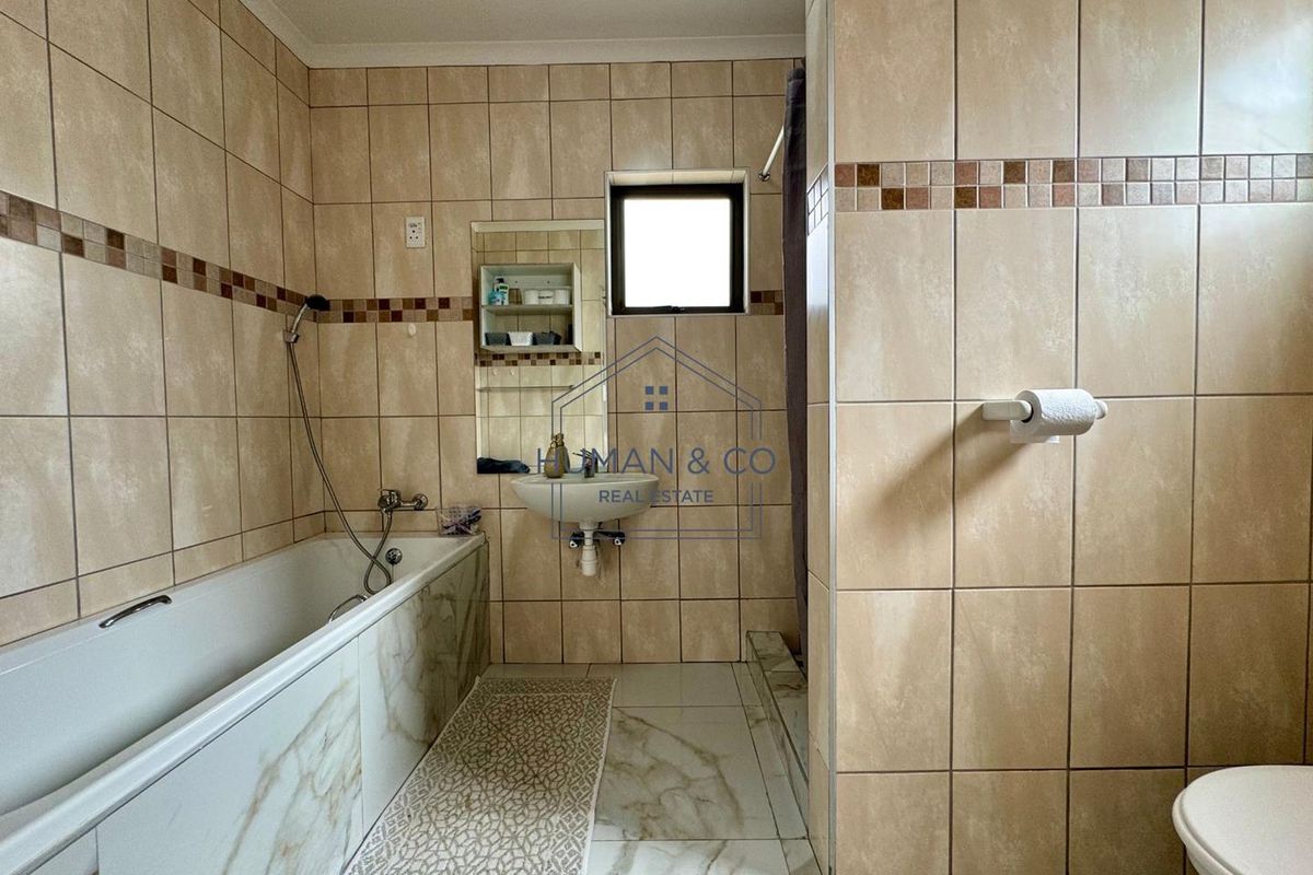 A functional bathroom featuring a bathtub, wall-mounted basin, and toilet with neutral floor-to-ceiling wall tiling.