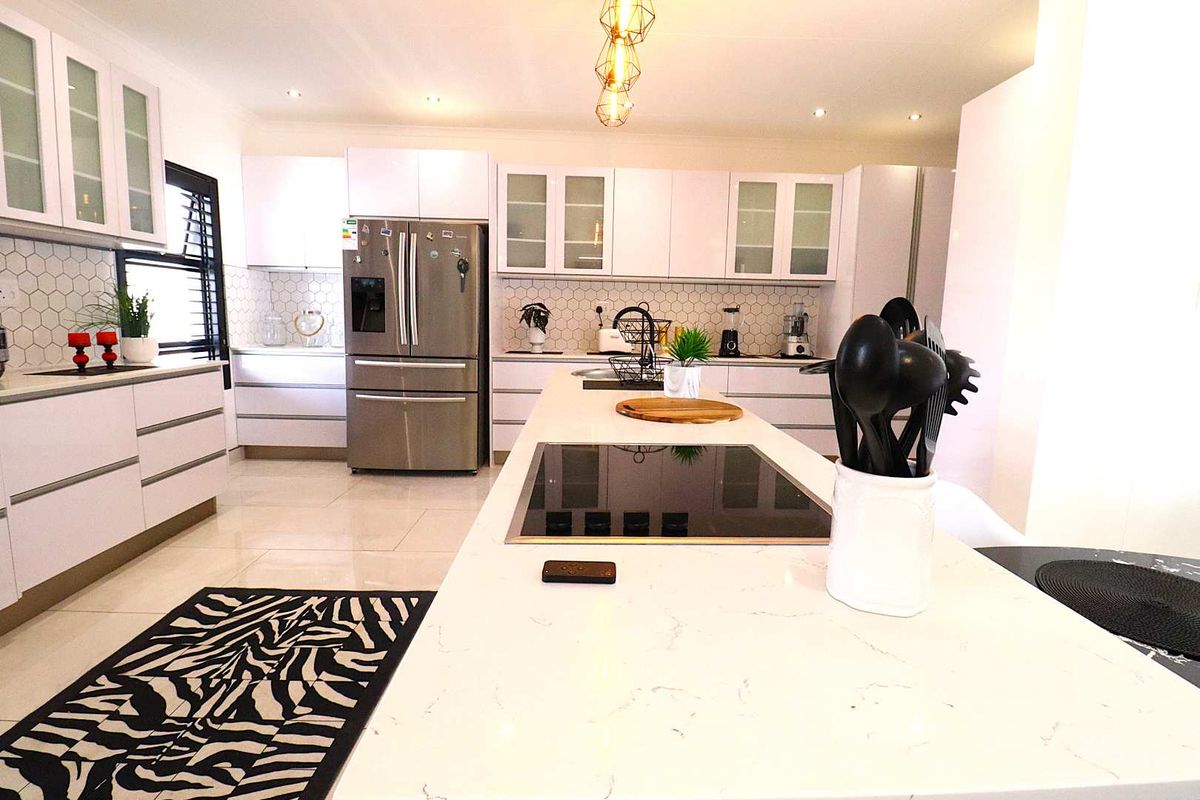 Modern kitchen featuring a central island with integrated induction hob, white cabinetry, stone countertops, and a hexagonal tile backsplash.