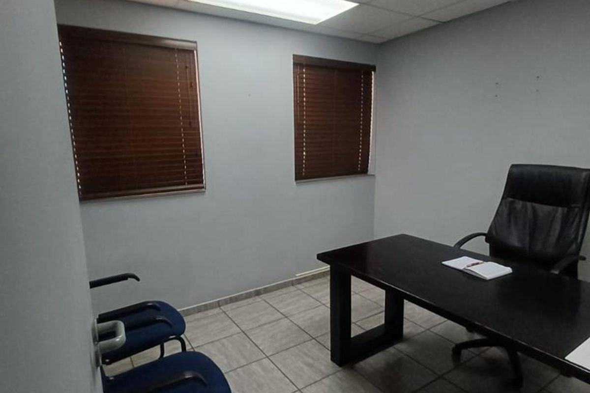 A functional office space featuring tiled flooring, a suspended ceiling with recessed lighting, and two windows fitted with venetian blinds.