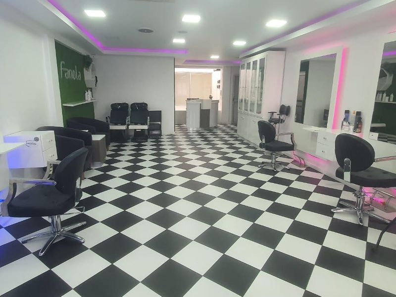 A well-maintained commercial salon space featuring checkered flooring, recessed lighting, built-in cabinetry, and wall-mounted mirrors with integrated LED accent lighting.