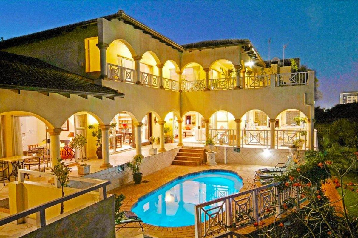 A spacious two-story rear exterior view featuring a swimming pool, covered patio areas, and arched architectural detailing.