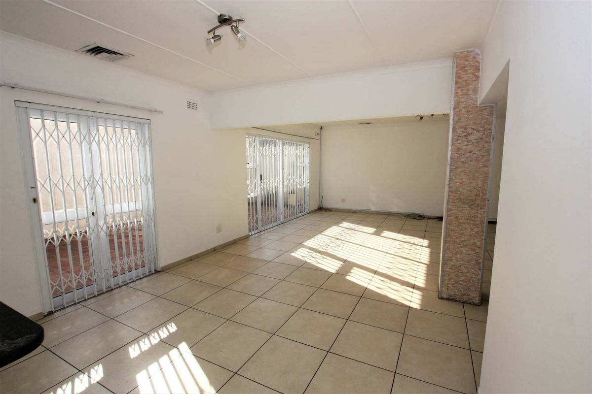 Spacious, empty living area featuring neutral floor tiles, security gates on sliding doors, and a decorative stone-clad pillar.