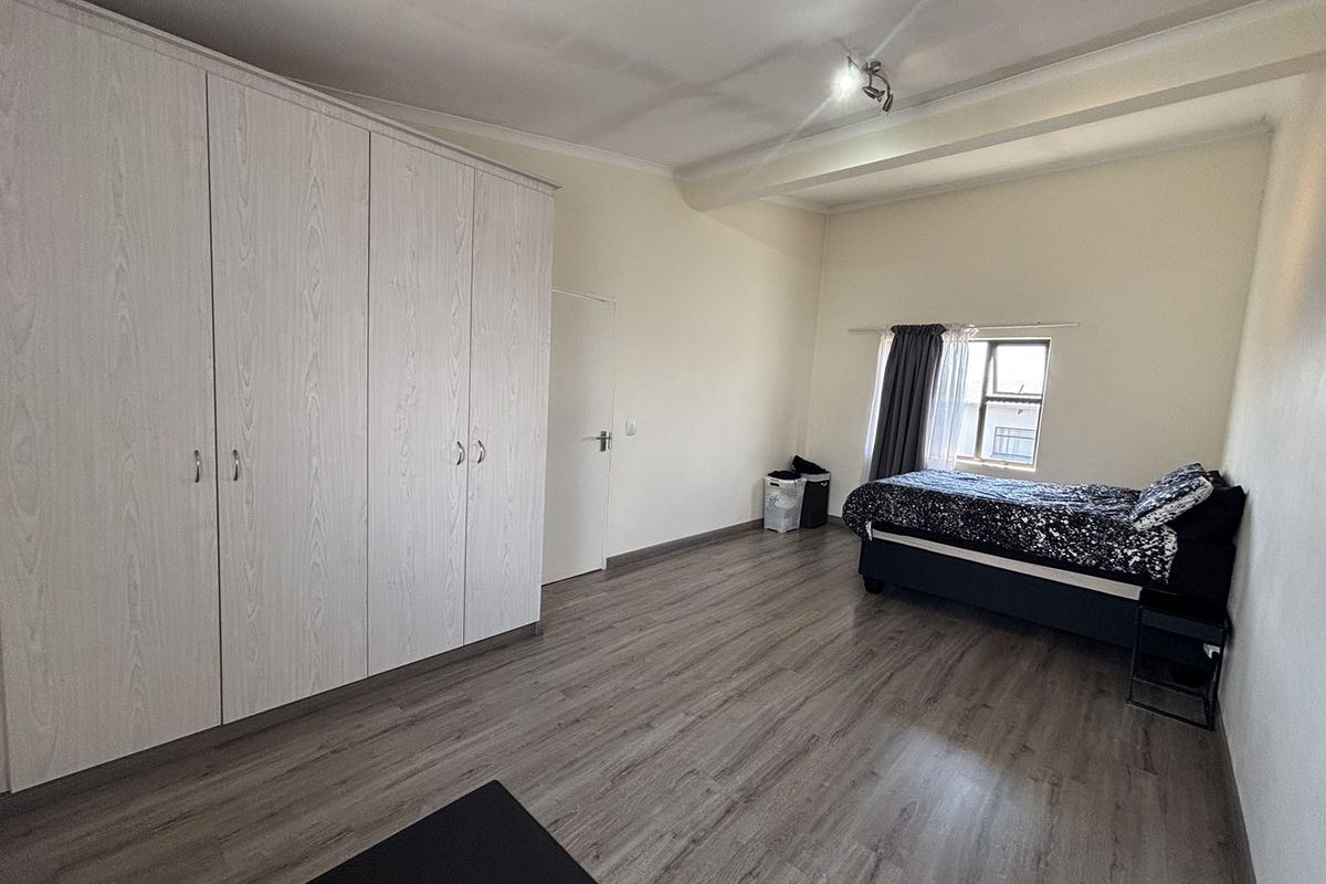 Spacious bedroom featuring light-toned laminate flooring and extensive built-in cupboard storage, offering a clean and functional living space.