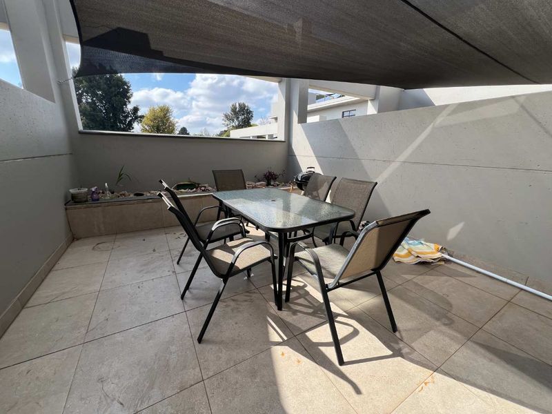 A private balcony featuring tiled flooring, a built-in planter box, and a shade sail, providing a functional outdoor entertainment space.