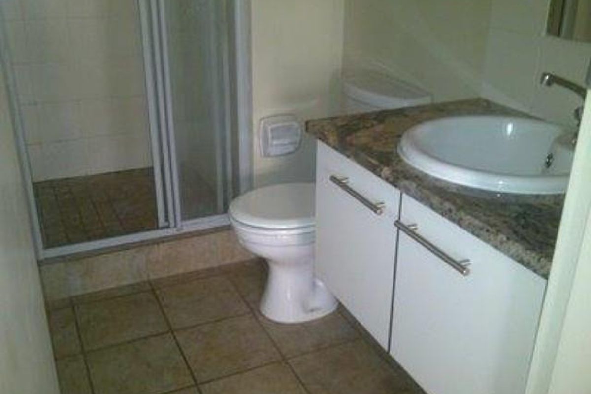 A functional bathroom featuring a shower enclosure, a white toilet, and a vanity unit with a granite countertop and integrated basin.