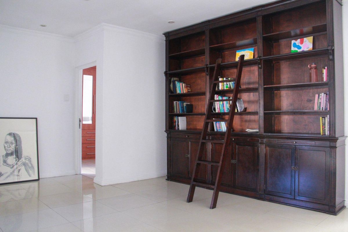 A spacious living area featuring a large, built-in dark wood library shelving unit with an integrated rolling ladder and polished tile flooring.