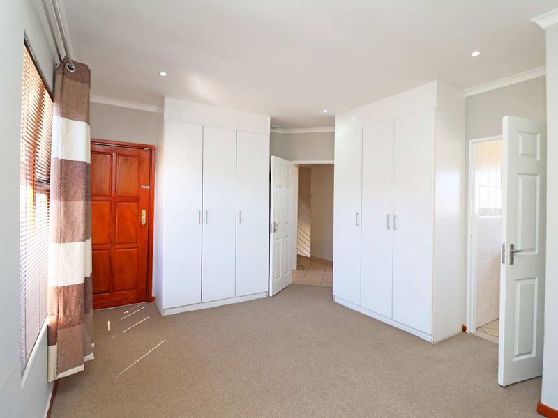 A bright, empty bedroom featuring neutral carpeting, ample built-in cupboard storage, recessed lighting, and direct access to an adjoining room.