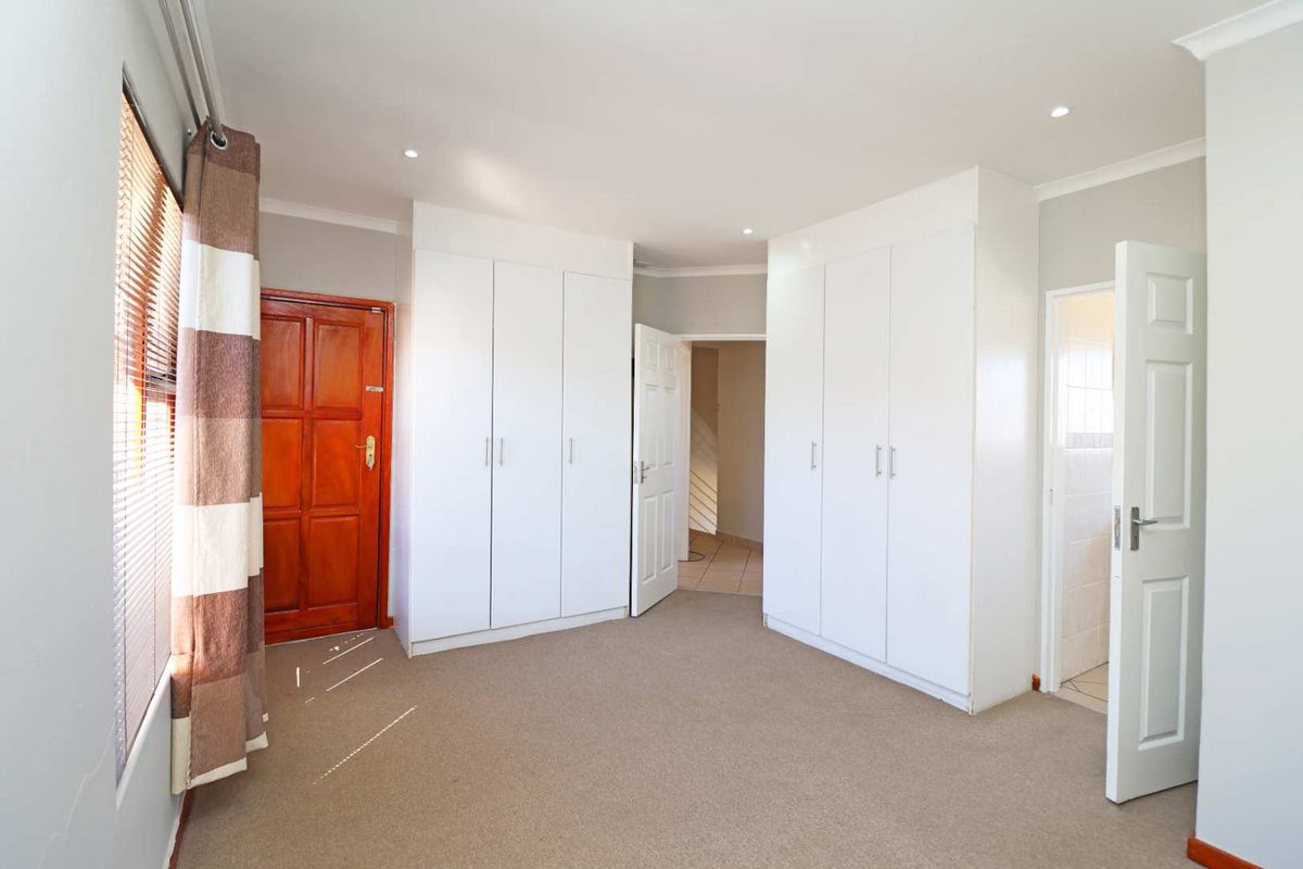 A bright, empty bedroom featuring neutral carpeting, ample built-in cupboard storage, recessed lighting, and direct access to an adjoining room.