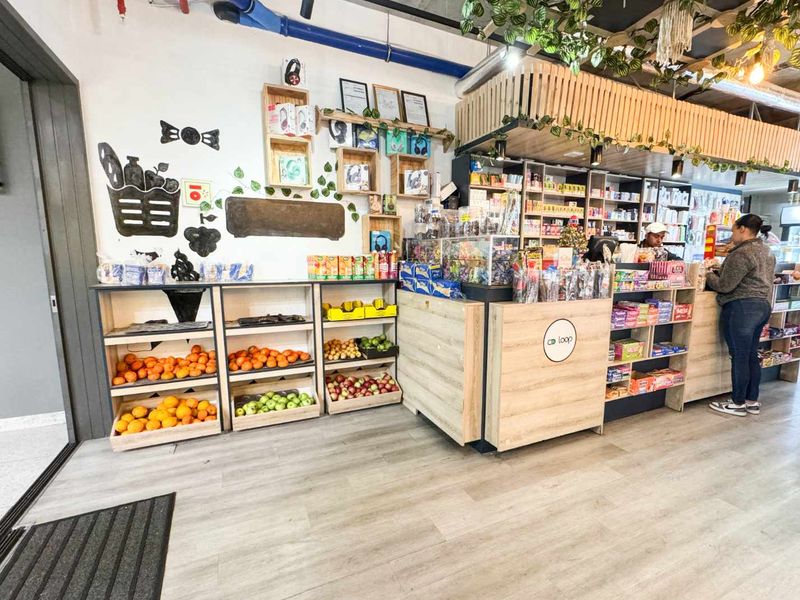 A retail space featuring a service counter, built-in wooden display shelving, laminate flooring, and an industrial-style exposed ceiling with decorative timber slats.