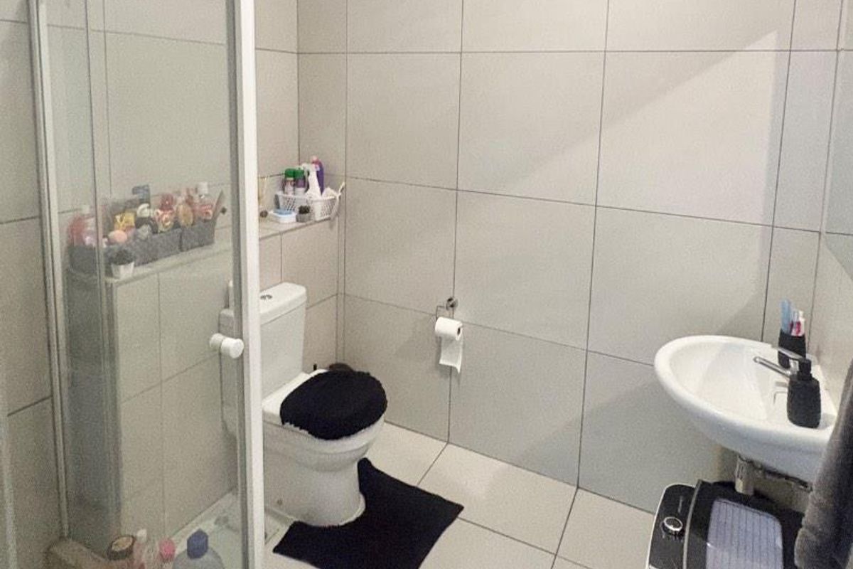 A functional bathroom featuring floor-to-ceiling wall tiles, a glass-enclosed shower, a pedestal basin, and a standard toilet.