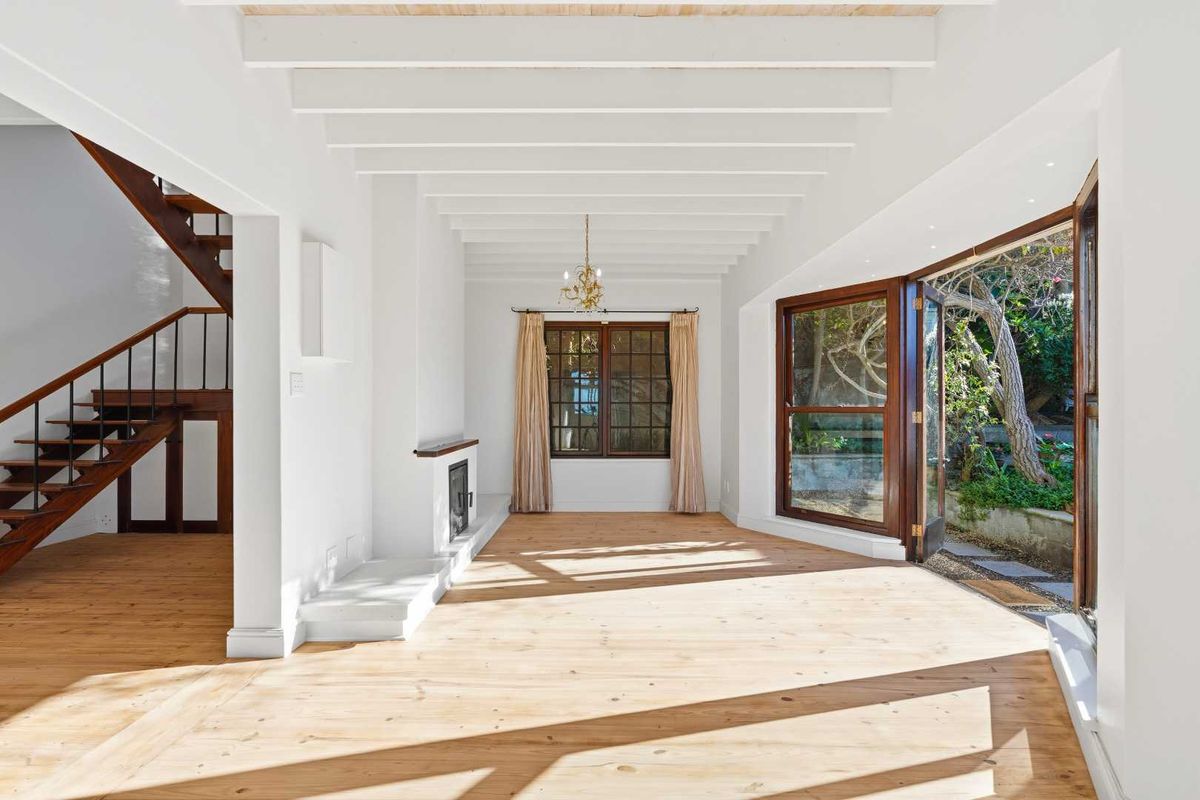 Bright and spacious living area featuring exposed timber ceiling beams, polished wooden flooring, a built-in fireplace, and direct access to the garden through folding doors.