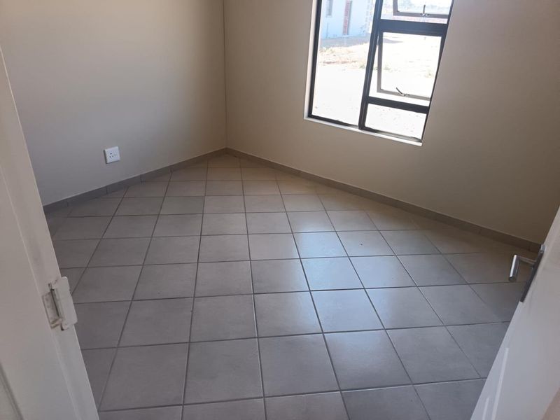 A clean, empty bedroom featuring neutral wall paint, tiled flooring, and a modern aluminium window frame.