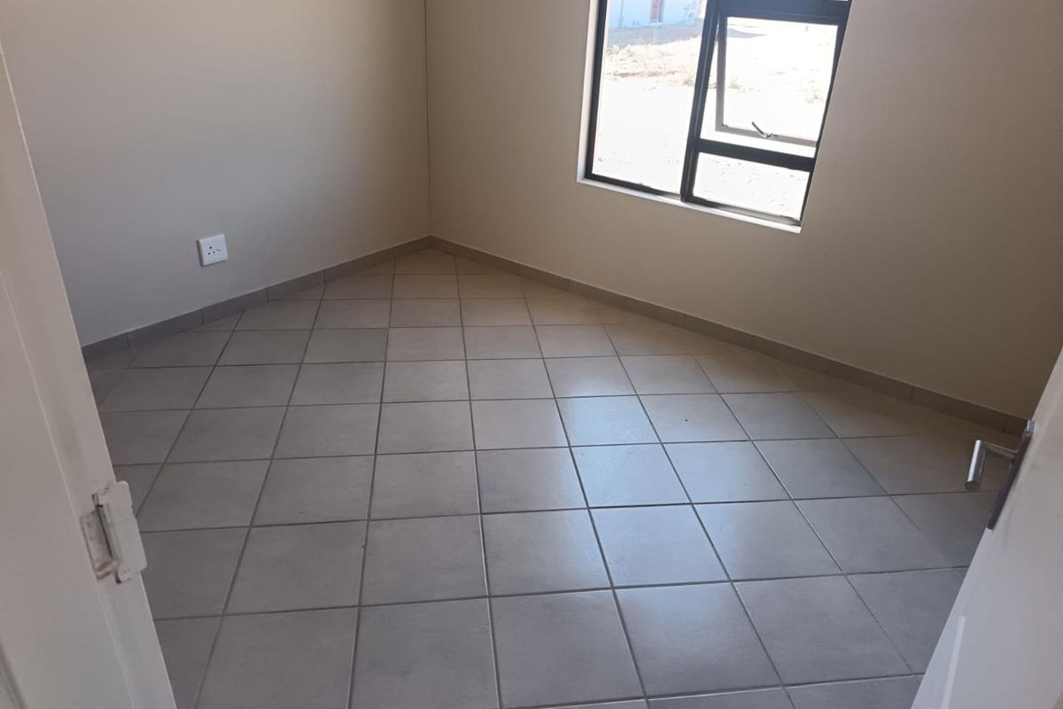 A clean, empty bedroom featuring neutral wall paint, tiled flooring, and a modern aluminium window frame.