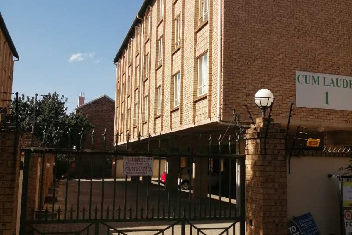 Exterior view of the apartment complex entrance featuring a brick facade, secure gated access, and paved driveway.